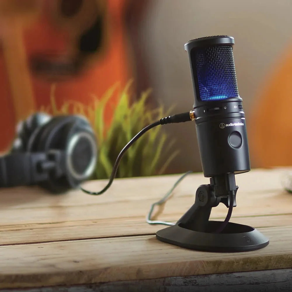 USB condenser microphone on desk stand with blue-lit grille, recording setup
