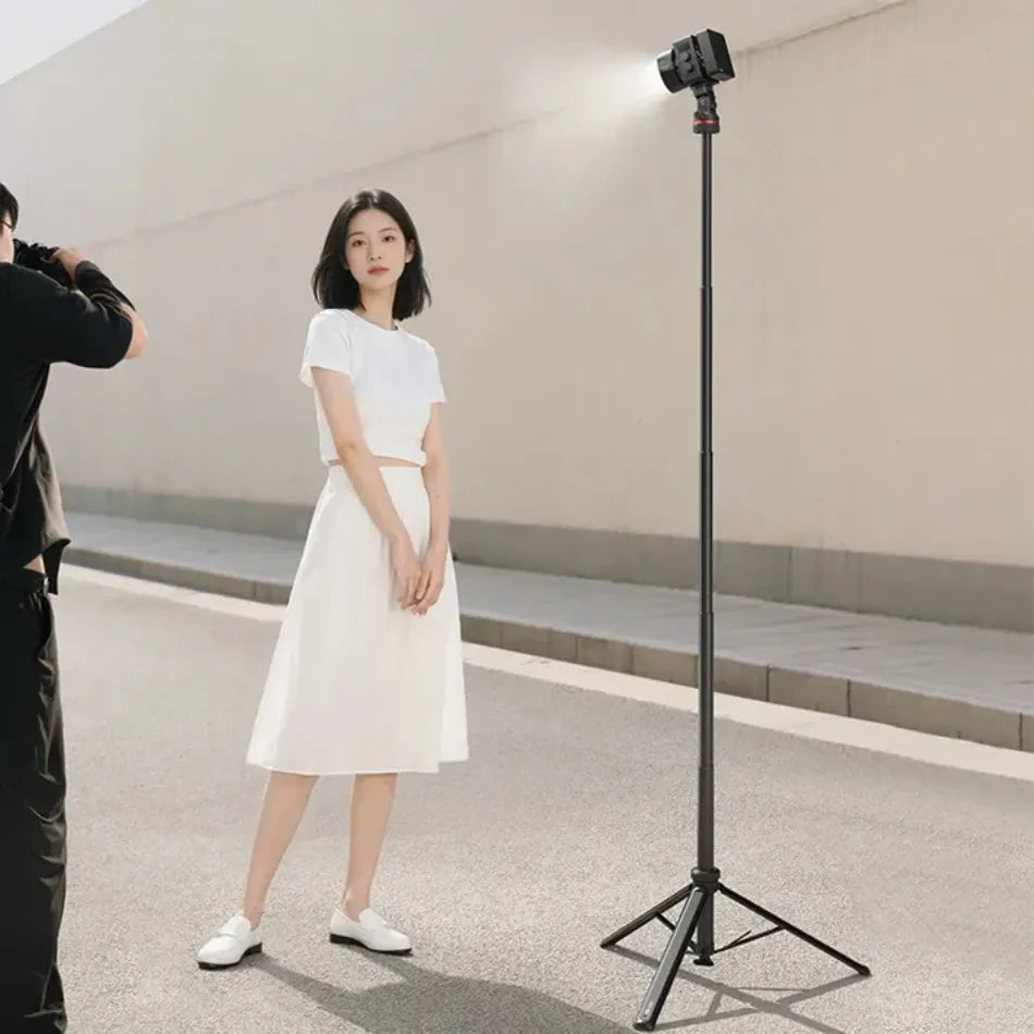 Woman in a white dress standing next to a photography with Ulanzi MT-80 Auto Open Tripod Light Stand   in an indoor setting.