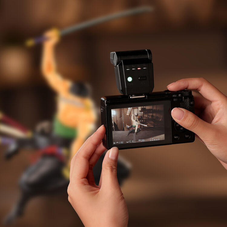 Black external camera flash mounted on a compact camera held in hands
